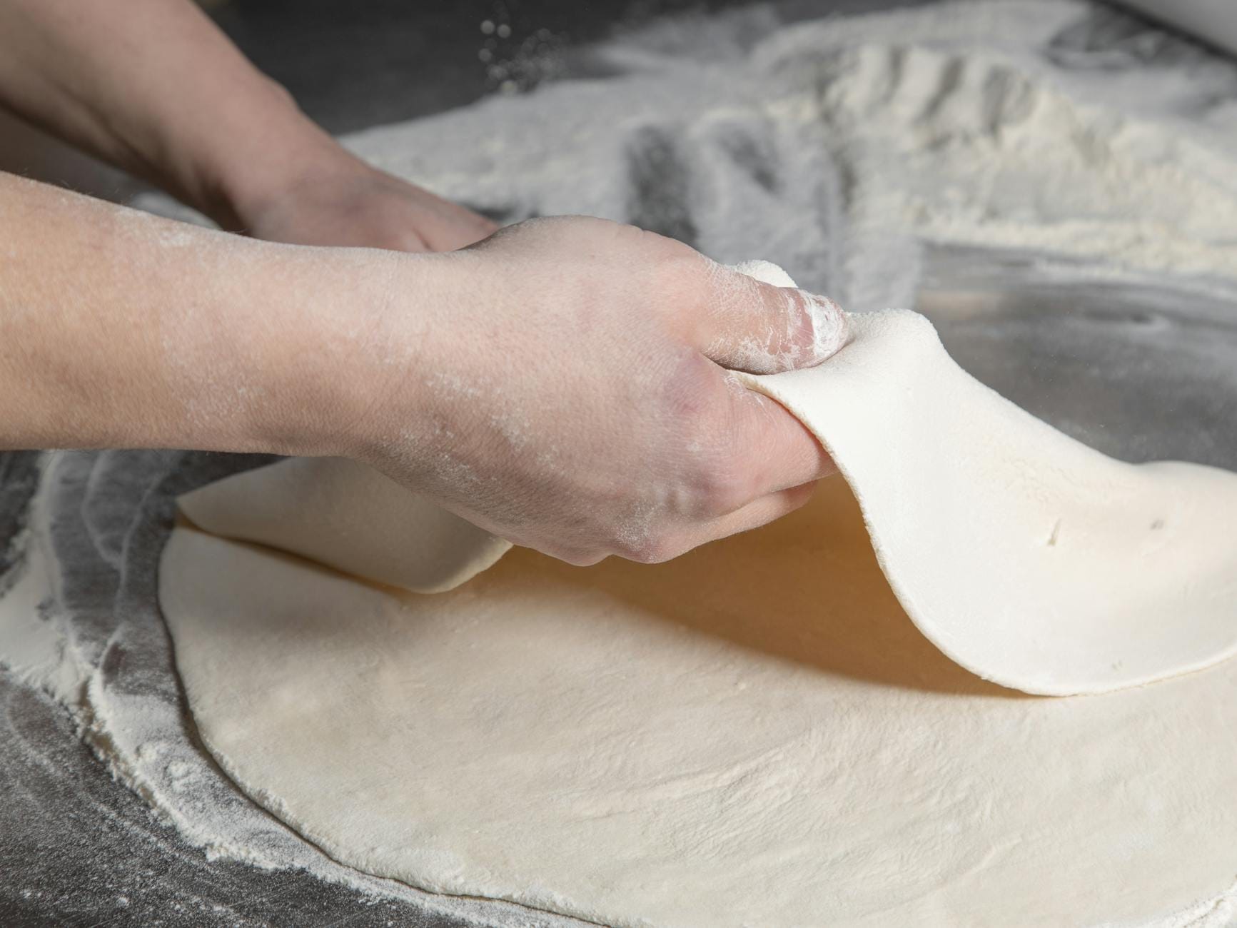 Jak dobra mąka do pizzy wpływa na smak, strukturę i wypiek w domowym piecu Dłonie wyrabiające ciasto na pizzę na oprószonym mąką blacie