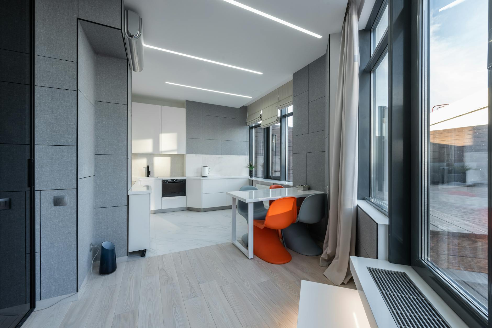 Wnętrza inspirowane modernizmem Gdyni: jak przenieść architekturę do mieszkania Jasny salon z kolorowymi krzesłami i szarą ścianą przy nowoczesnej kuchni