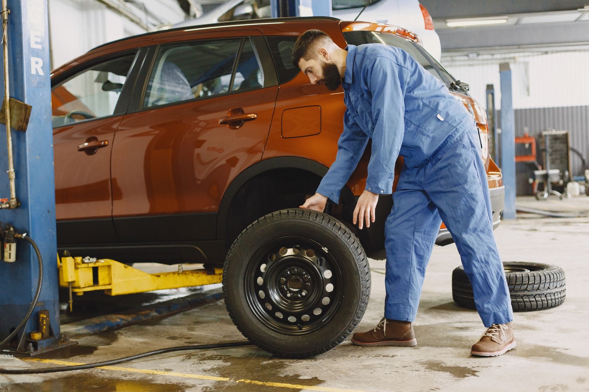 Mechanik w niebieskim kombinezonie wymienia koło w czerwonym SUV-ie w warsztacie